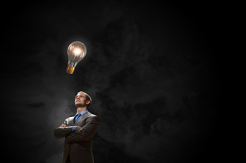 Young confident businessman with arms crossed on chest looking at light bulb