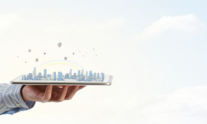 Hand holding tablet computer with cityscape on screen