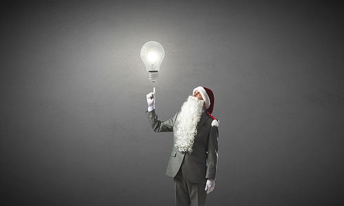 Thoughtful businessman in Santa pointing at light bulb