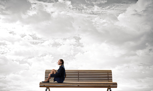 Bored young businesswoman sitting alone on wooden bench