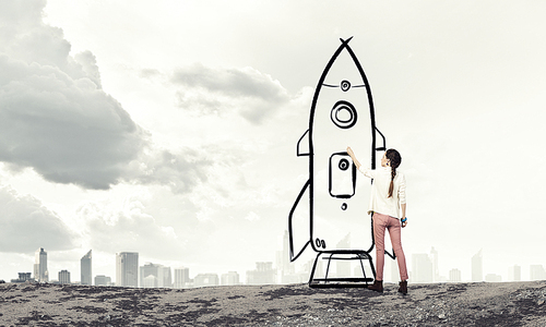 Young student girl standing with back and drawing rocket