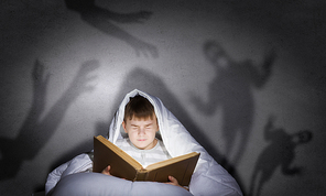 Little scared boy in bed under blanket with flashlight