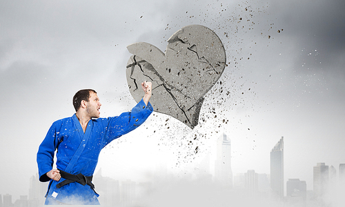 Young determined karate man breaking with hand concrete heart