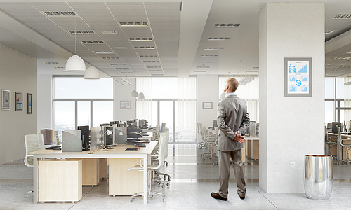 Thoughtful businessman standing with back in empty office