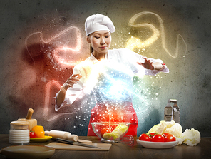 Asian female cooking with magic against color background