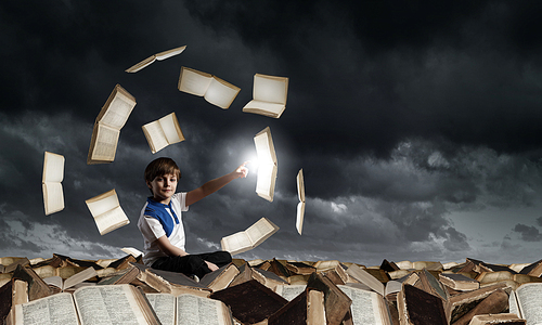 Little cute boy sitting on pile of books and pointing with finger