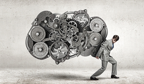 Young businessman carrying huge gears mechanism on back