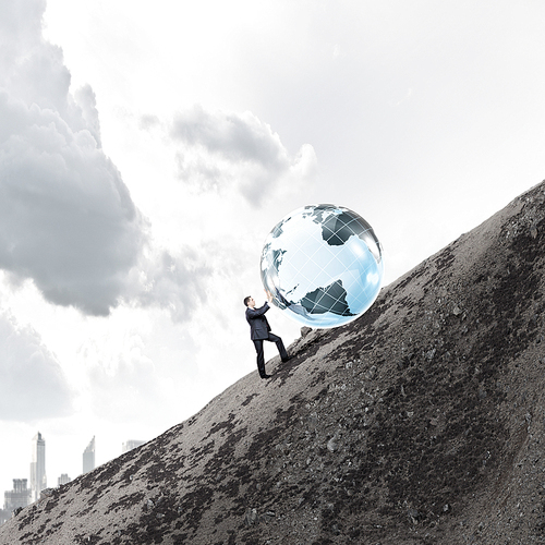 Businessman rolling Earth planet up the hill