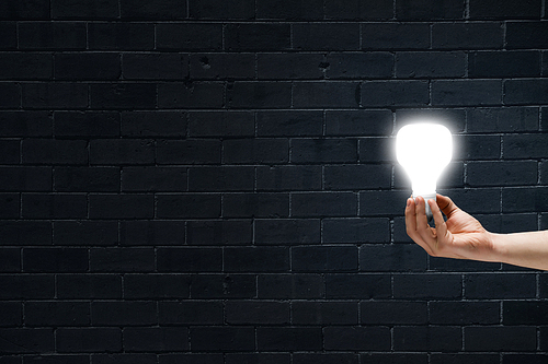 Male hand on dark background showing glass light bulb