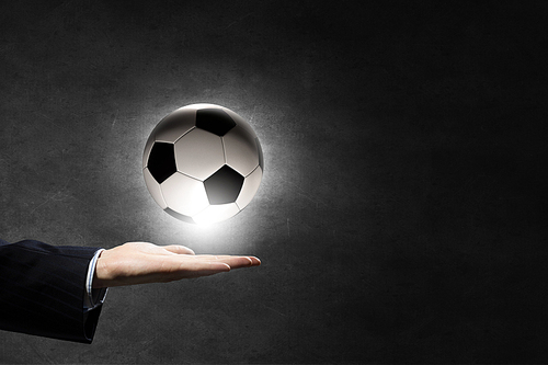Hand of businessman on dark background holding soccer ball