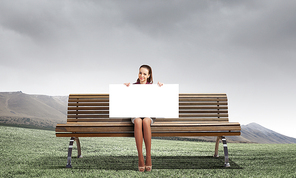 Young woman with white blank banner sitting on bench