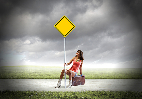 Young pretty girl traveler sitting on suitcase aside of road