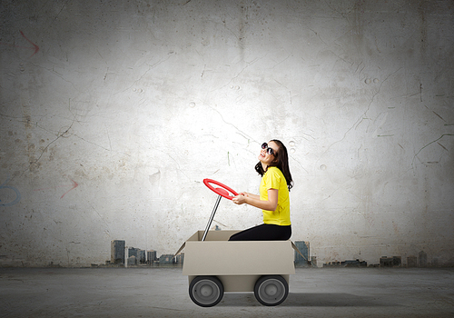 Young funny woman riding in carton box