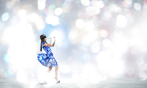 Young woman in blue dress wearing blindfold and playing fife