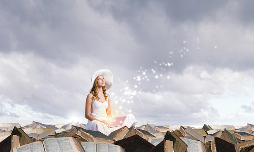 Young lady sitting on pile of books with laptop