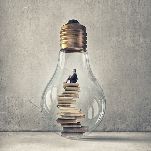 Young woman sitting om books stack inside of glass light bulb