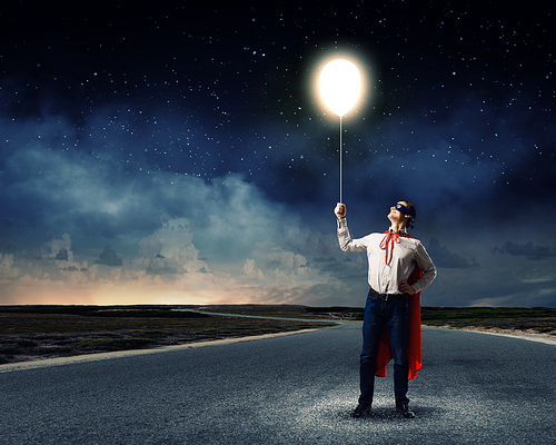 Young man in superhero costume holding balloon in hand