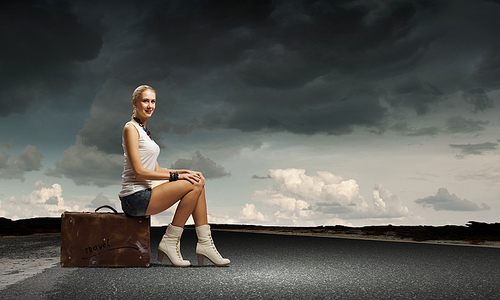 Young woman hiker sitting on suitcase along roadside