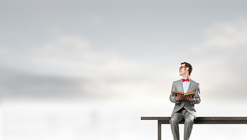 Young businessman wearing red bow tie sitting on bench with book in hands