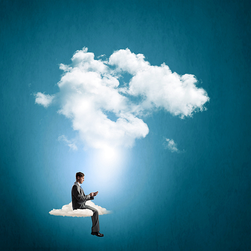 Young businessman sitting on cloud with mobile phone in hands