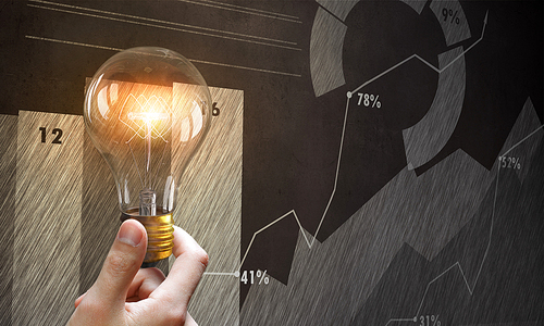 Male hand holding light bulb on background of diagrams and graphs