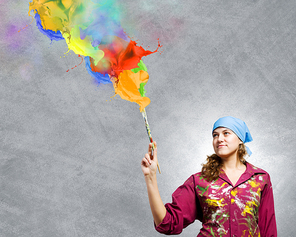 Young woman painter with brush and colorful splashes above