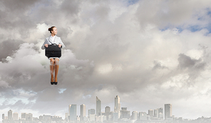 Young pretty businesswoman sitting on cloud high above city