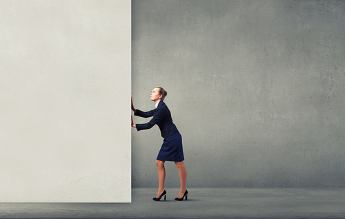 Young businesswoman making effort to move wall