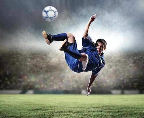 football player in blue shirt striking the ball aloft at the stadium