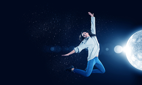 Young woman dancer jumping in spotlights on dark background