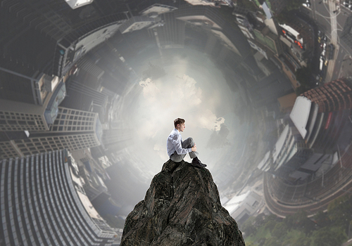 Young thoughtful businessman sitting alone on rock top