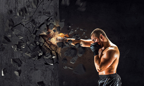 Strong boxer man in gloves breaking cement wall