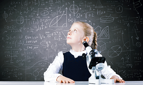 Cute school girl with microscope in classroom