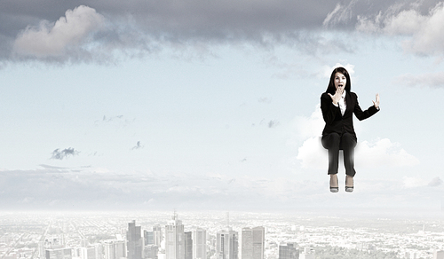 Young emotional businesswoman sitting on cloud above city