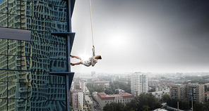 Concept of competition with businesswoman climbing office building with rope