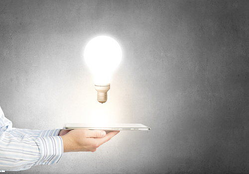 Human hands holding tablet pc with light bulb on it