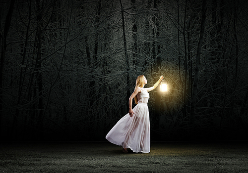Young woman with lantern walking in dark forest