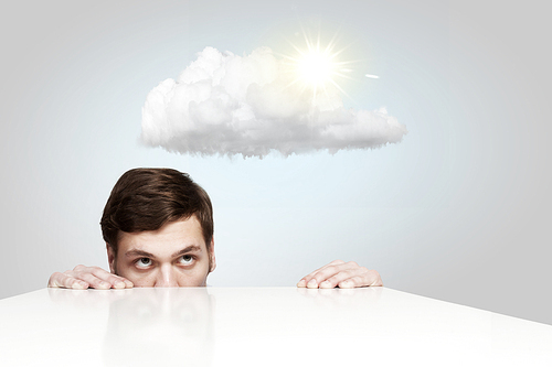 Young businessman looking from under table at sun behind cloud