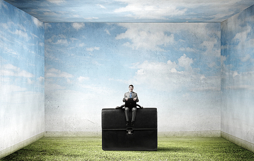 Young smiling businessman sitting on giant briefcase