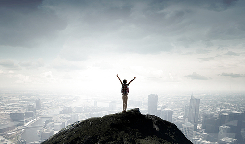 Rear view of girl with hands up facing sunrise abone city