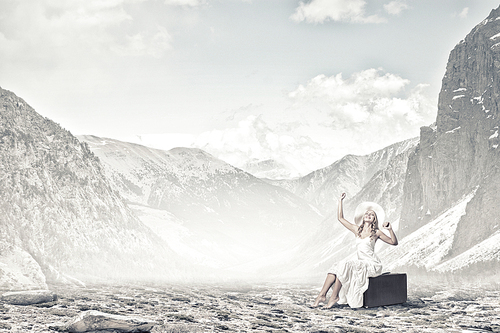 Woman in white long dress and hat sitting on her luggage