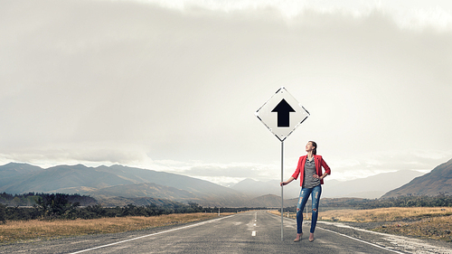 Young girl in red jacket on road showing roadsign