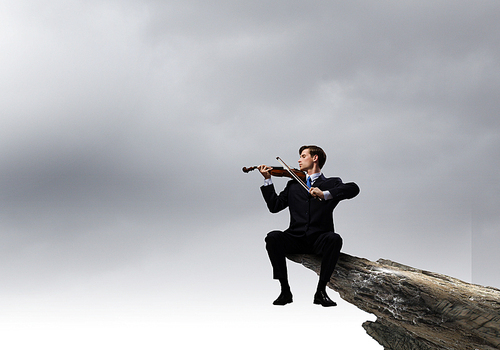 Businessman sitting on rock edge and playing violin