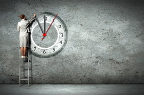Businesswoman standing on ladder moving hands of clock