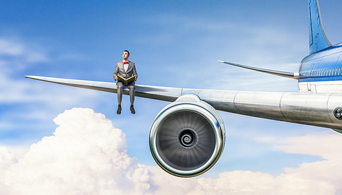Young businessman sitting on wing of airplane and reading book