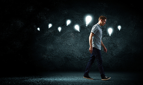 Young man and electrical bulb against dark background