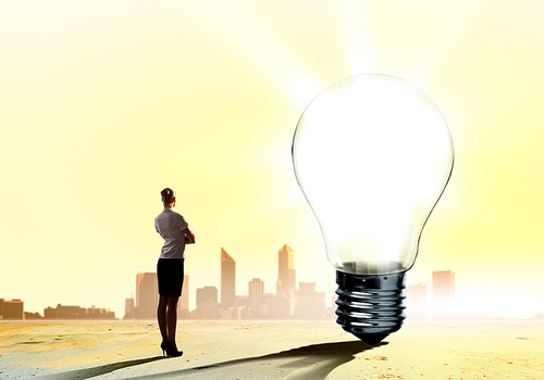 Image of businesswoman looking at light bulb. Green energy concept