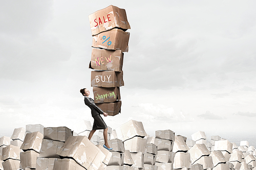 Attractive businesswoman carrying big stack of carton boxes