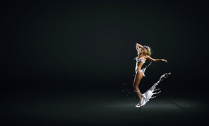 Hot young dancing woman in white bikini on dark background