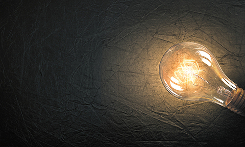 Power and energy concept with glass glowing light bulb on concrete backdrop